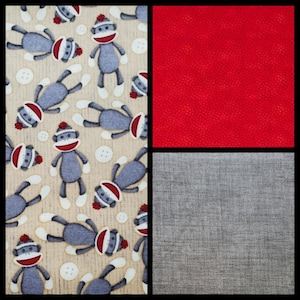 May include: A fabric panel featuring a repeating pattern of sock monkey characters in gray, red, and white on a tan background. White buttons are scattered throughout. The image also includes solid red and gray fabric swatches.