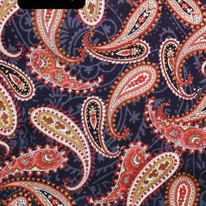 May include: A black fabric with a paisley pattern in shades of red, orange, and cream. The fabric is measured with a ruler in inches.