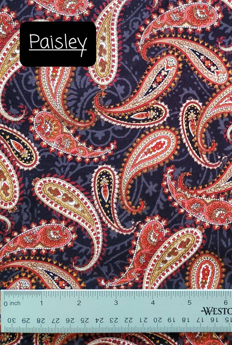 May include: A black fabric with a paisley pattern in shades of red, orange, and cream. The fabric is measured with a ruler in inches.