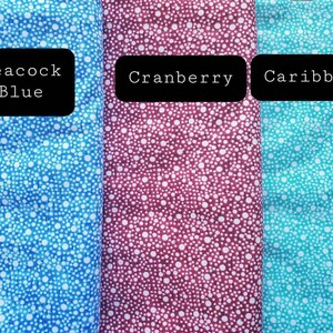 May include: Three fabric swatches with a white polka dot pattern on a blue, burgundy, and turquoise background. The swatches are labeled "Peacock Blue", "Cranberry", and "Caribbean".