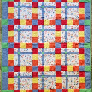 May include: A patchwork quilt with a grid pattern of red, yellow, blue, and white fabric. The quilt is made of squares and rectangles, and the fabric has a variety of patterns, including polka dots, stripes, and a pattern of children playing.