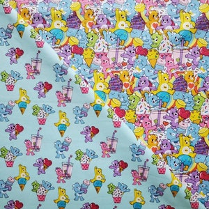 May include: A blue fabric with a repeating pattern of cartoon bears holding ice cream cones, drinks, and cupcakes. The bears are in various colors, including pink, purple, yellow, and blue.