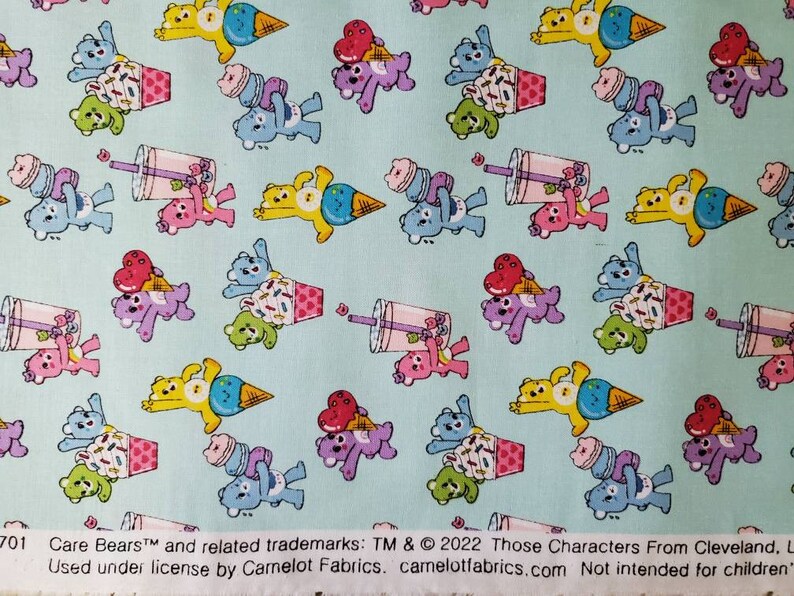 May include: A light blue fabric with a repeating pattern of Care Bears characters. The bears are holding ice cream cones and cups of bubble tea. The text "Care Bears&trade; and related trademarks: TM & &copy; 2022 Those Characters From Cleveland, L. Used under license by Camelot Fabrics. camelotfabrics.com Not intended for children." is printed at the bottom of the fabric.
