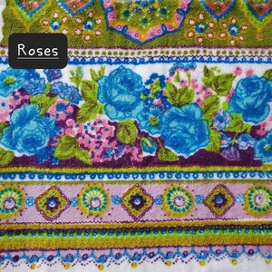 May include: A white towel with a colourful floral pattern. The pattern features blue roses, green leaves, and pink flowers. The towel has a border of green, purple, and pink.