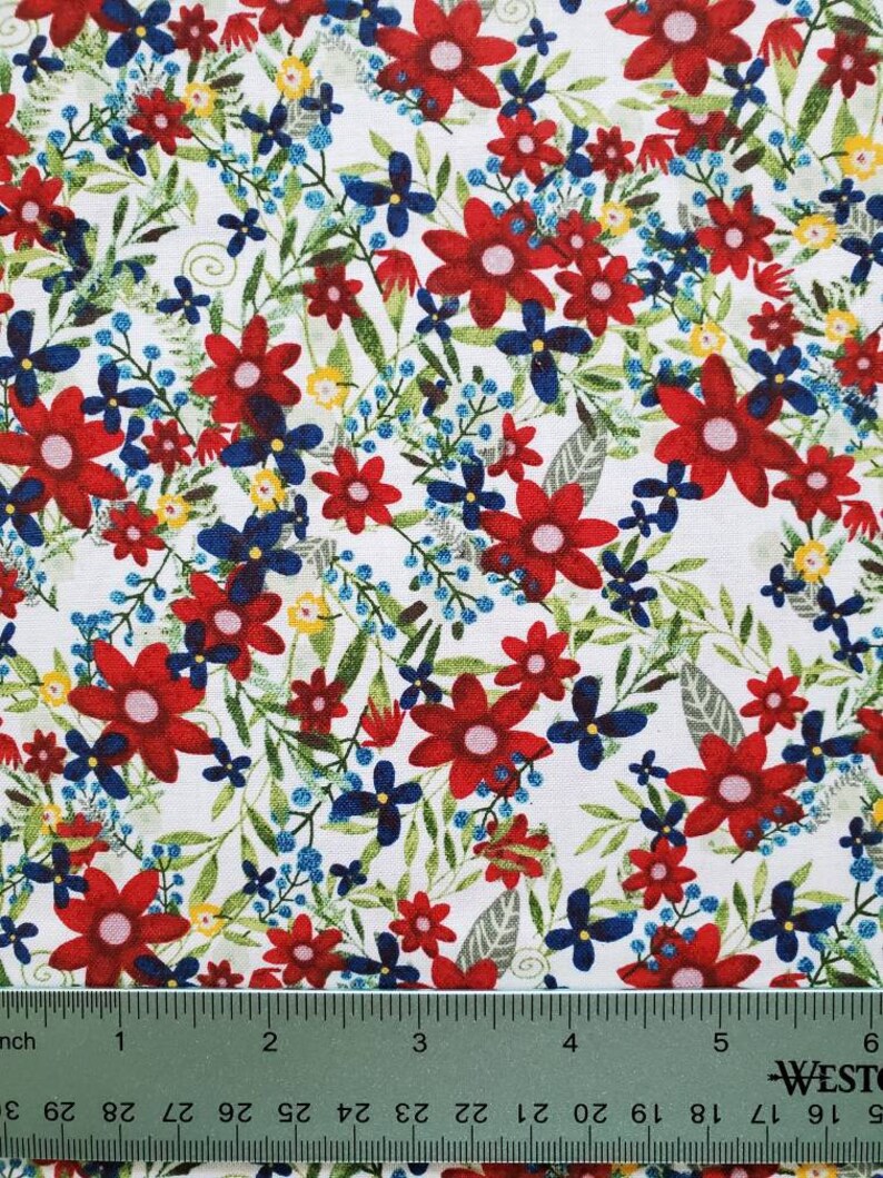 May include: White fabric with a red, blue, and yellow floral pattern. The fabric is shown with a ruler for scale.