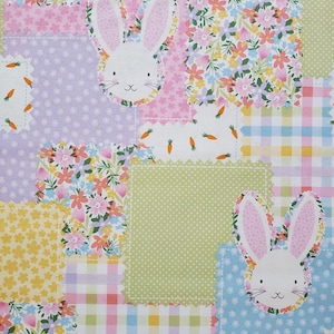 May include: A patchwork fabric design featuring bunny faces and floral patterns. The squares are in pastel colors like pink, blue, yellow, and green, with white bunnies and carrot accents. The fabric has a scalloped edge.