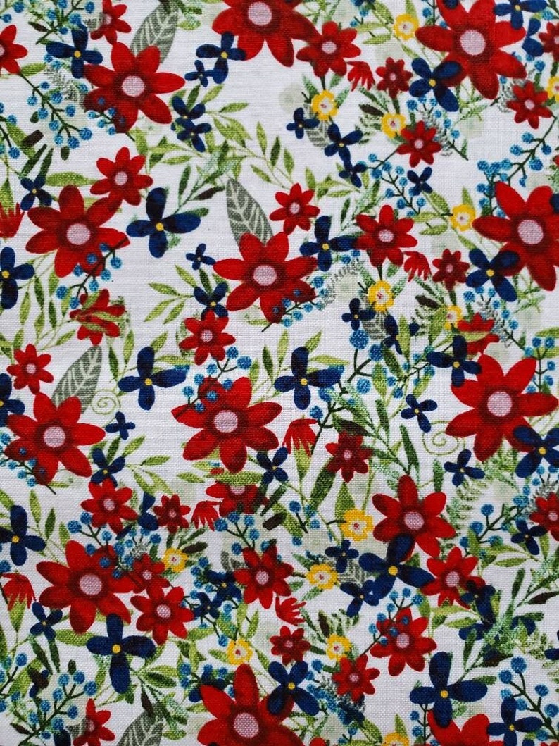 May include: A white fabric with a red, blue, and yellow floral pattern. The fabric features a variety of flower shapes and sizes, including large red flowers with white centers and smaller blue and yellow flowers.