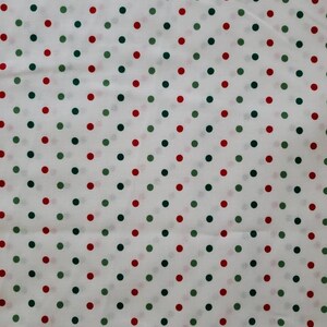 May include: White fabric with a repeating pattern of red and green polka dots. The dots are evenly spaced and arranged in a diagonal grid across the fabric's surface. The fabric appears to be lightweight.