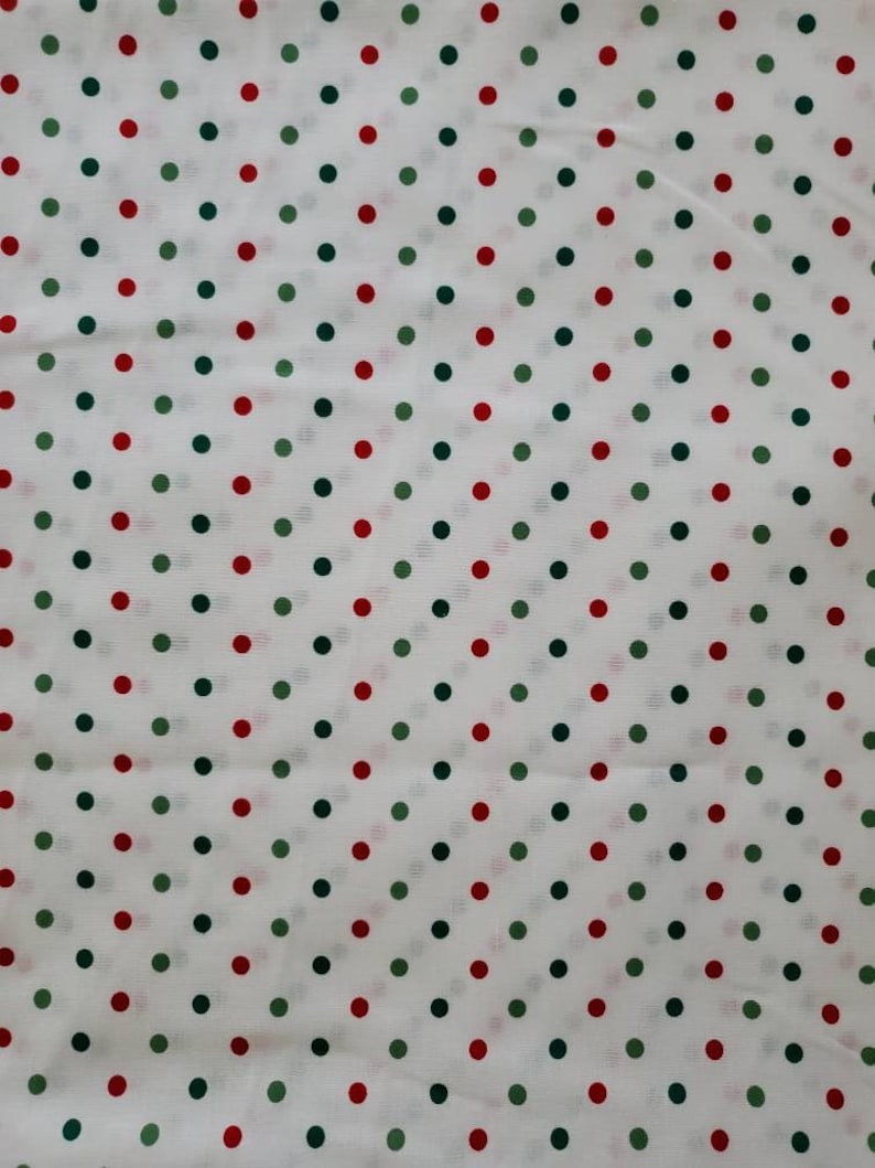 May include: White fabric with a repeating pattern of red and green polka dots. The dots are evenly spaced and arranged in a diagonal grid across the fabric's surface. The fabric appears to be lightweight.
