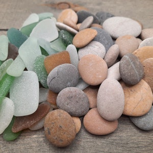 Può includere: Una collezione di pietre lisce e vetro di mare consumato dal mare in tonalità di verde, marrone e bianco. Le pietre sono di varie dimensioni e forme, alcune con una texture ruvida.