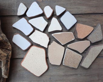 May include: A collection of irregular shaped ceramic tiles in various shades of brown, beige, and white. The tiles are arranged in a random pattern on a wooden surface.