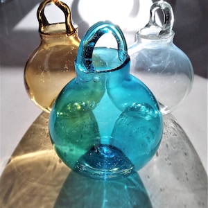 May include: Three glass bottles with handles. The bottle on the left is amber, the bottle in the center is blue-green, and the bottle on the right is clear.
