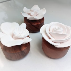 Peut inclure: Trois diffuseurs de fleurs en céramique blanche, chacun reposant sur une base en bois. Les fleurs sont une rose, une orchidée et un magnolia.