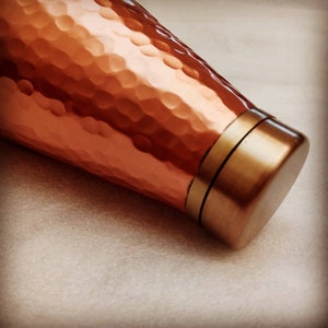 May include: A copper water bottle with a hammered finish and a gold-colored lid.