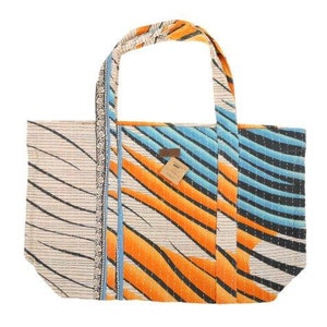 May include: A large, white tote bag with a blue and orange geometric pattern. The bag has a brown leather tag with the word "WOVEN" on it.