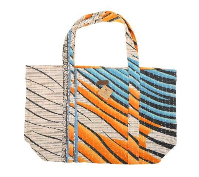 May include: A large, white tote bag with a blue and orange geometric pattern. The bag has a brown leather tag with the word "WOVEN" on it.