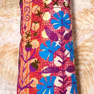 May include: A long rectangular pillow with a colorful floral pattern. The pillow is embroidered with blue, purple, orange, and green flowers on a red background.