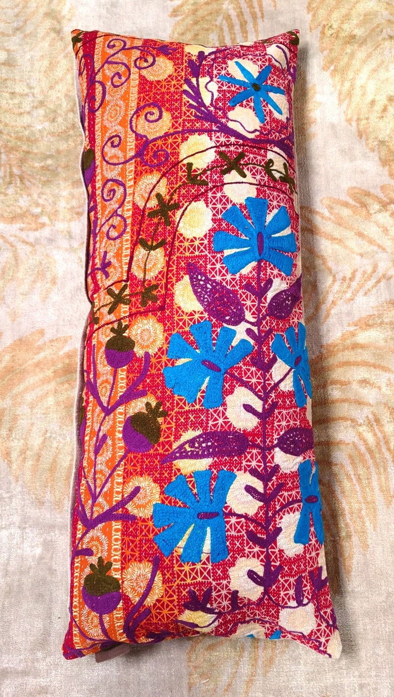 May include: A long rectangular pillow with a colorful floral pattern. The pillow is embroidered with blue, purple, orange, and green flowers on a red background.