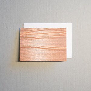 May include: A wooden card with a natural wood grain pattern. The card is light brown with a white border.