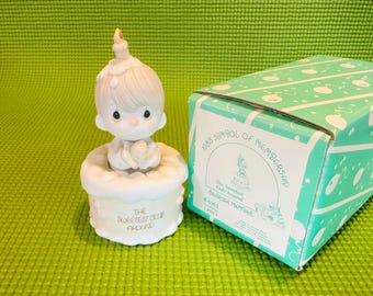 May include: A white porcelain figurine of a cherubic child with blonde hair wearing a white dress and holding a small white bird. The figurine is sitting on a white cake with the words "The Sweetest Club Around" written on it. The figurine is in a box with the words "988 Symbol of Membership" and "The Sweetest Club Around Charter Member" written on it.