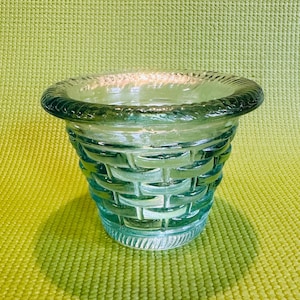May include: A light blue glass planter with a woven design. The planter is empty and sitting on a green surface.