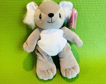 May include: A plush koala bear toy with gray fur, white accents, and a smiling face. The koala has large, fluffy ears and a white belly. It is positioned on a textured green surface.