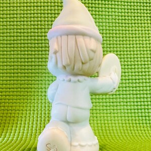 May include: A white porcelain figurine of a little girl wearing a blue and white dress and a white hat. She is holding a cymbal in her right hand. The figurine is signed "Sam" on the bottom.