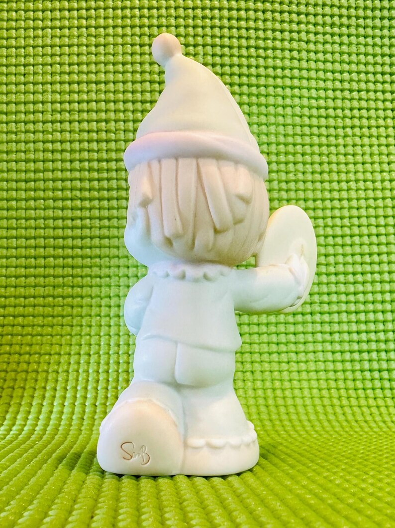 May include: A white porcelain figurine of a little girl wearing a blue and white dress and a white hat. She is holding a cymbal in her right hand. The figurine is signed "Sam" on the bottom.