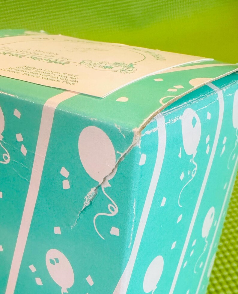 May include: A turquoise blue gift box with a white label that reads "A Classic Series by The Country Rose Collection". The box is decorated with white balloons and confetti.