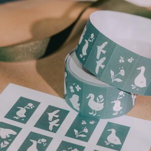 May include: A roll of teal adhesive labels and a matching sheet of rectangular stickers, both featuring a repeating white graphic pattern of ducks, birds, and small flowers. The stickers are arranged in a grid on the sheet and on the roll.