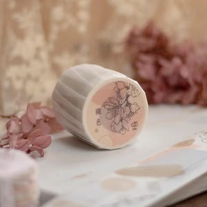 May include: A roll of decorative washi tape with a floral design and the text "櫻色" in Japanese. The tape is pink and white with a delicate floral pattern.