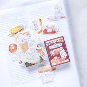 May include: A selection of quirky stickers depicting chefs, pastries, and kitchen utensils. The stickers include a recipe book with the text "magic recipe boulangerie". The colour scheme incorporates browns, reds, and white.