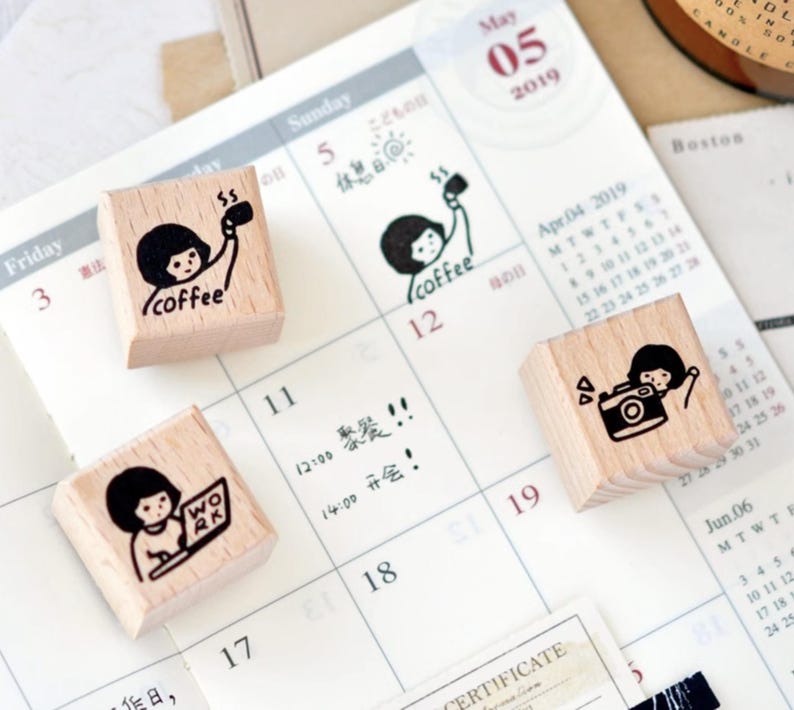 Puede incluir: Cuatro sellos de madera con ilustraciones en tinta negra sobre un calendario. Un sello dice "coffee", otro muestra a una persona con una taza de caf&eacute;, un tercero muestra a una persona con una c&aacute;mara y el &uacute;ltimo muestra a una persona trabajando en una computadora port&aacute;til.