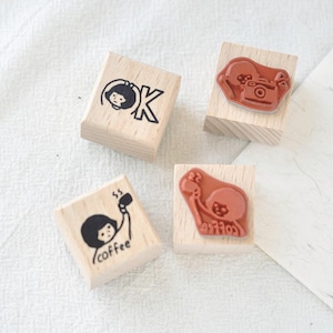 Puede incluir: Cuatro sellos de madera con dise&ntilde;os de tinta negra. Un sello tiene una persona con la palabra "OK", otro tiene una c&aacute;mara, un tercero tiene una persona con una taza de caf&eacute; y la palabra "coffee", y el &uacute;ltimo tiene una persona con una c&aacute;mara.