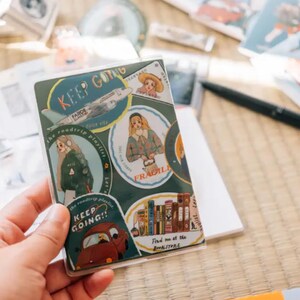 May include: A sheet of stickers with various illustrations and text. The stickers feature a plane, a book, a girl with a book, a girl with a backpack, and a car. The text on the stickers includes "Keep Going", "The Wanderlust Playlist", "Fragile", and "Find me at the Bookstore".