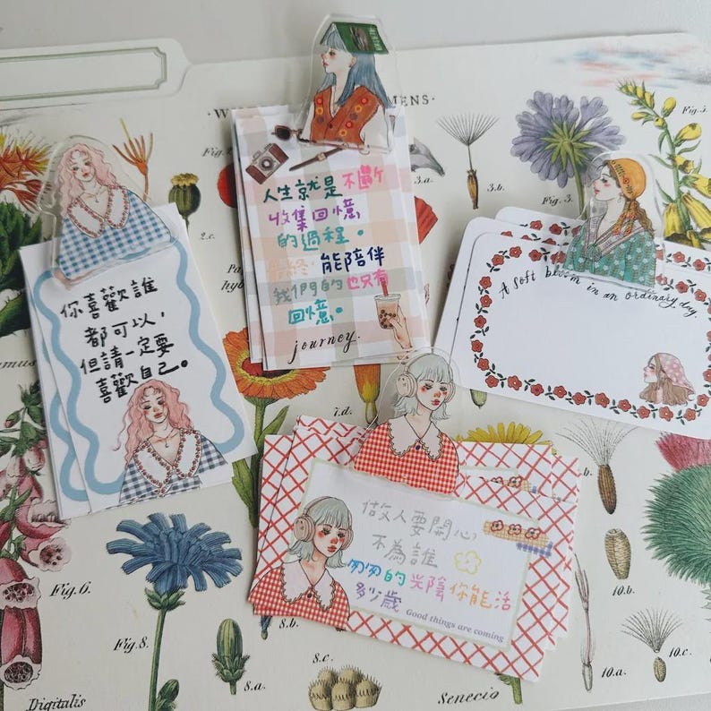 May include: Decorative paper cards and bookmarks with illustrations of women and handwritten text. The cards feature floral and plaid patterns, with phrases like "A soft bloom in an ordinary day" and Chinese text.