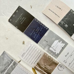 May include: A collection of decorative paper strips with various designs and text. The strips feature quotes like "Love yourself first" and "Work, but don't forget to live." Colors include black, blue, brown, and gray. Some strips have a receipt or to-do list layout.