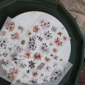 May include: Two sheets of clear sticker paper with floral designs. The stickers feature pink and white flowers with black outlines. The stickers are on a white background.