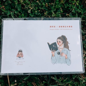 May include: A white card with a black and white illustration of a woman reading a book. The text on the card reads "Passport Holder / L/W Notebook Cover".