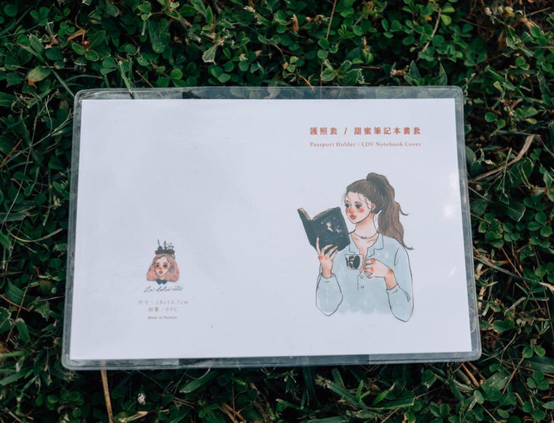 May include: A white card with a black and white illustration of a woman reading a book. The text on the card reads "Passport Holder / L/W Notebook Cover".