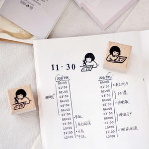 Puede incluir: Sellos de madera con un dise&ntilde;o de ni&ntilde;a de dibujos animados, ideales para hacer un diario o planificar. Los sellos muestran a la ni&ntilde;a escribiendo y la palabra "WORK". La imagen tambi&eacute;n muestra una p&aacute;gina de planificador con horarios escritos a mano y caracteres chinos.
