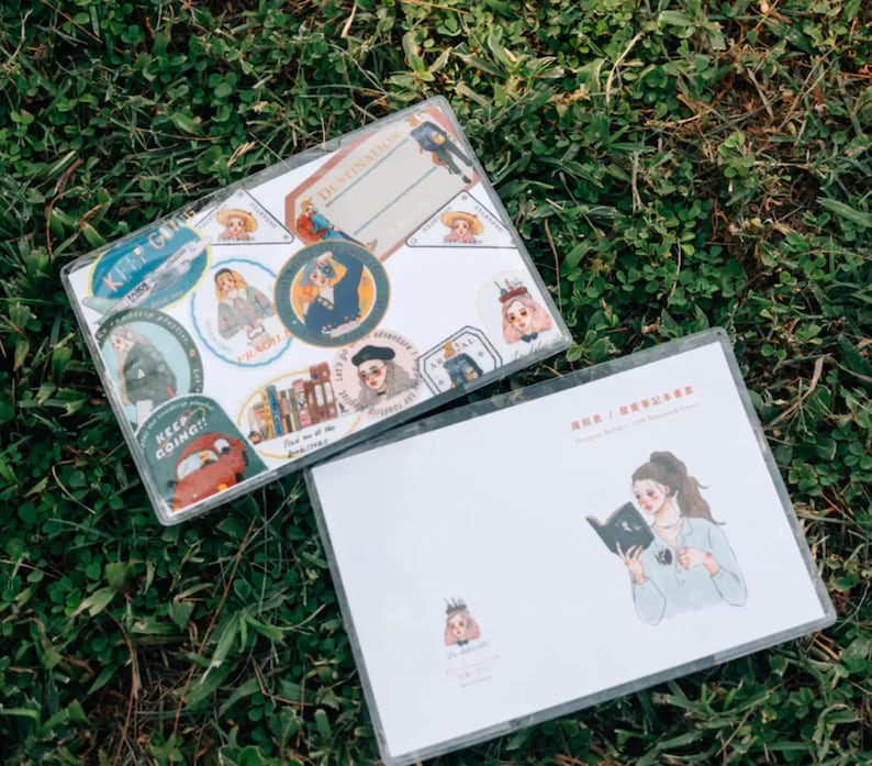 May include: Two clear plastic sheets with colorful stickers and illustrations. The top sheet has stickers with text like "Keep Going!" and "Destinations". The bottom sheet has a drawing of a person reading a book.