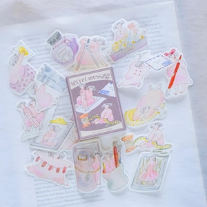 May include: A set of 15 clear stickers featuring illustrations of people in various scenes. The stickers are printed on a white background and have a matte finish. The stickers are packaged in a small box with the text "Secret Message" printed on the front. The stickers are ideal for adding a touch of whimsy to journals, planners, and other paper crafts.
