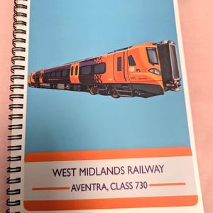 Può includere: Quaderno a spirale con un'illustrazione di un treno arancione e viola su sfondo blu. La copertina mostra il testo "WEST MIDLANDS RAILWAY AVENTRA, CLASS 730" in bianco e arancione.