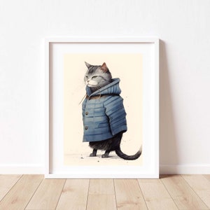 May include: A framed art print featuring a grey tabby cat wearing a blue hooded duffle coat with brown toggle buttons. The cat is depicted in a standing position, facing to the left, against a light cream-coloured background with subtle speckles.
