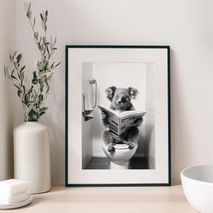 Puede incluir: Una l&aacute;mina de arte mural en blanco y negro enmarcada que muestra a un koala sentado en un inodoro leyendo un peri&oacute;dico. El koala est&aacute; situado en un ba&ntilde;o con azulejos. La l&aacute;mina est&aacute; dentro de un marco negro sencillo con un paspart&uacute; blanco.