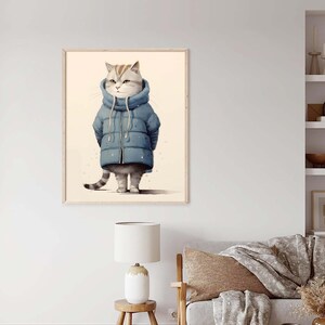 May include: A framed wall art print featuring a light-colored cat with tabby markings wearing a blue puffer jacket with a high collar and drawstrings. The cat stands upright against a plain, light-colored background, showcasing its striped tail.