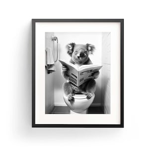 Puede incluir: Una impresi&oacute;n art&iacute;stica enmarcada en blanco y negro que muestra a un koala sentado en un inodoro blanco mientras lee un peri&oacute;dico abierto. El koala tiene orejas esponjosas y est&aacute; en un ba&ntilde;o con azulejos y una toalla colgada en la pared.