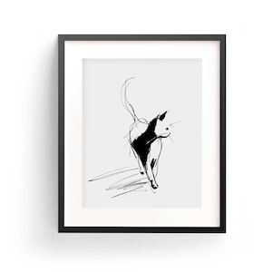 Pode incluir: Esboço a preto e branco de um gato em movimento, emoldurado numa moldura preta. A obra de arte utiliza pinceladas arrojadas para capturar a forma e o movimento do gato sobre um fundo branco.