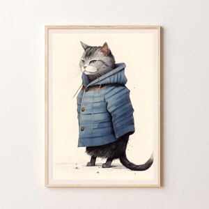 May include: A framed wall art print featuring a grey tabby cat wearing a blue hooded duffle coat with toggle buttons. The cat is depicted in profile, standing on a light cream background. The wooden frame surrounds the illustration.